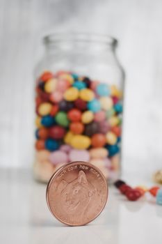 Digital currency physical brass dogecoin coin near sweets in glass jar.