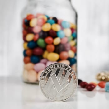 Digital currency physical silver Litecoin coin near sweets jar.