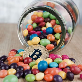 Digital currency physical gold bitcoin coin near colorful tasty sweets on the wooden board.