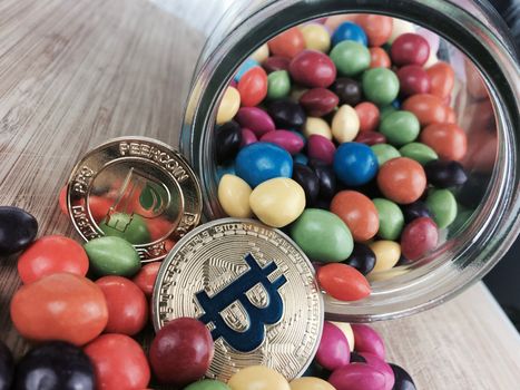 Digital currency physical gold bitcoin coin and peercoin near sweets in jar.