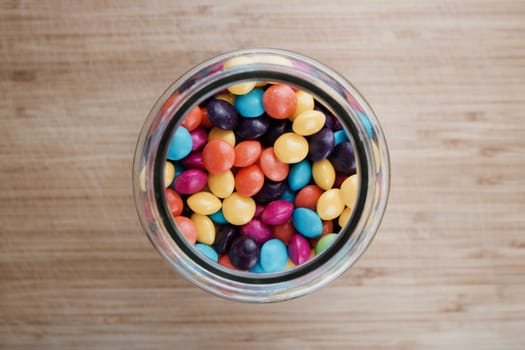 Tasty and colorful jelly sweets in glass jar on the wooden board in the kitchen.
