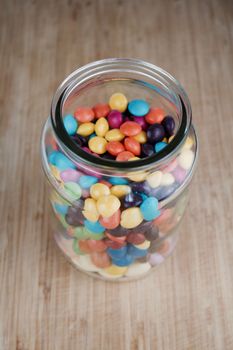 Tasty jelly colorful sweets in glass jar on the wooden board in the kitchen.