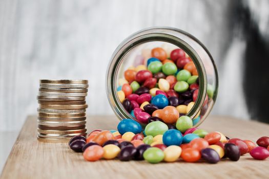 Money jar and colorful sweets on the wooden board in the kitchen.