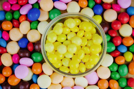 Small yellow sweets in the jar near colored sweets.
