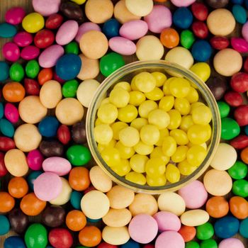 Tasty yellow jelly sweets in glass jar near colorfull candies.