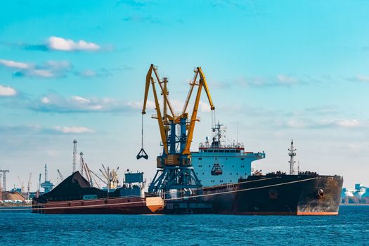 Black cargo ship loading with a coal at the port