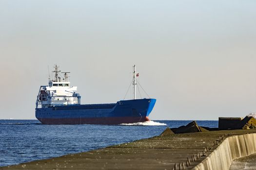 Blue cargo ship sailing against the breakwater dam