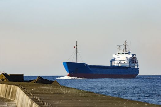 Blue cargo ship sailing against the breakwater dam