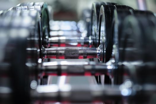 Spinlock dumbbells in special rack at gym, selective focus at one of plates