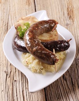 Blood sausage and white pudding with sauerkraut and baked potato on wooden background