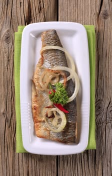 Pan fried trout on a white platter on wooden background