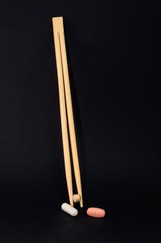 Chopsticks with tablets against a black background. Concept of health costs and drug misuse.