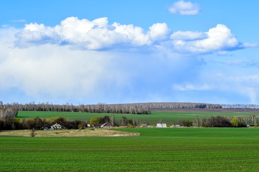Rural landscape with a green field, clouds and farm.