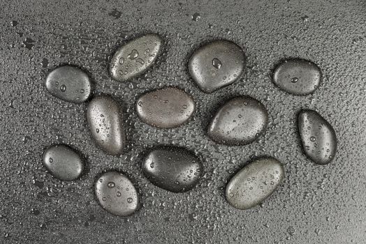 Several black basalt massage stones, covered with water drops, distributed on a black background; top view, flat lay