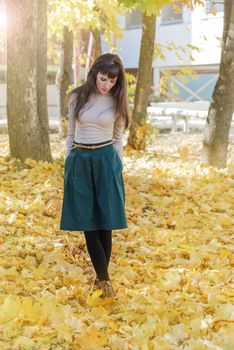 Slim brunette girl with long hair in a green skirt and beige turtleneck in autumn park