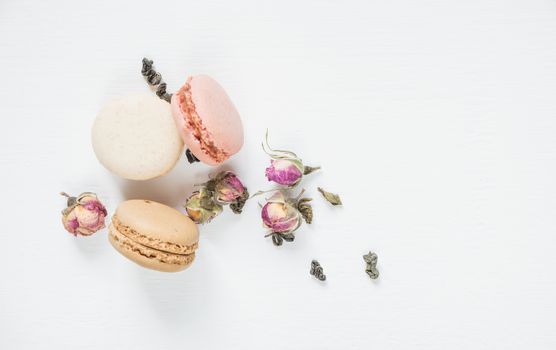 Traditional French multicoloured macaroons,d dried rose buds and green tea on white background; top view, flat lay