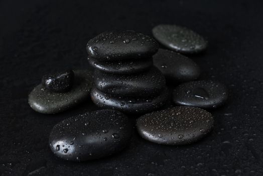 Spa concept with heap of the black basalt massage stones covered with water drops on a black background