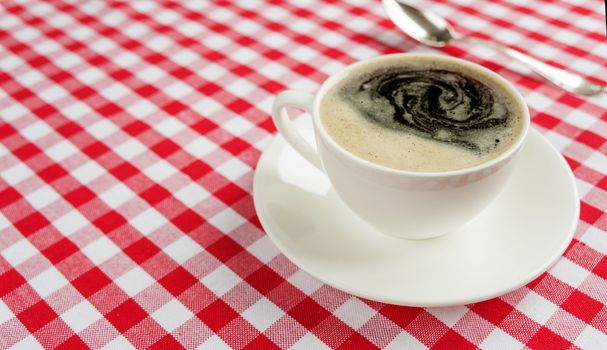 Strong black coffee in the white porcelain cup on a background of red and white checkered cloth