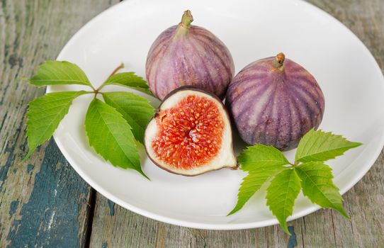 Ripe figs and beautiful green leaves are on a white porcelain plate