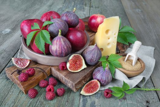 Ripe figs, red raspberry and apples, cane sugar and cheese are on old cutting board as well as green leaves lie on the old wooden table