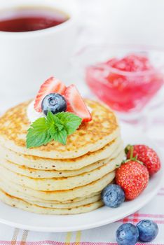 A stack of pancakes decorated with ripe raspberries, blueberries and sour cream close-up