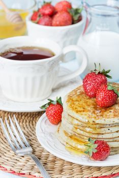 A stack of pancakes with honey decorated with ripe raspberries and a cup of tea