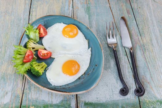 Breakfast consists of fried eggs and vegetables on the old wooden table, rustic style