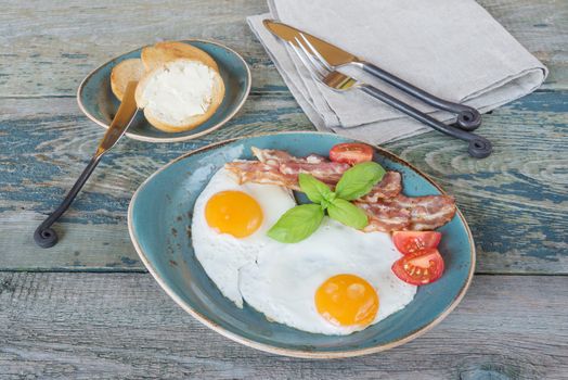 Breakfast consists of fried eggs,  bacon, tomato and toasts whith butter on the old wooden table; top view, flat lay