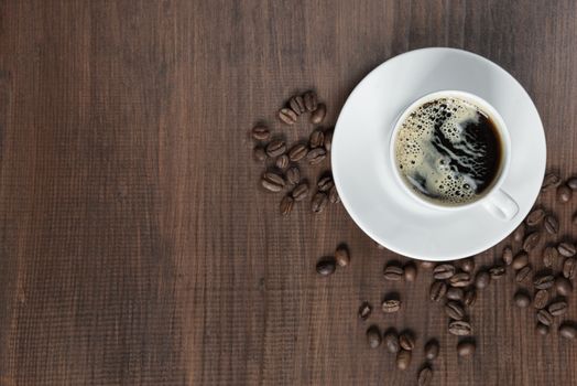 Cup of coffee on the wooden background with coffee beans; top view