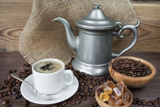 Cup of coffee, coffee pot and wooden bowl with sugar on the wooden background with coffee beans