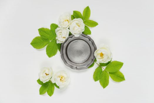 Decorative composition in retro style consisting of vintage metal tray ore retro plate and white rose flowers with green leaves on white background. Top view, flat lay