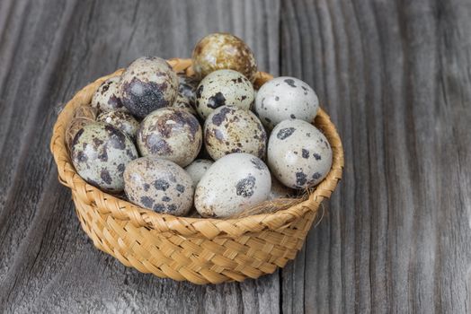 Several spotted quail eggs in a wicker basket on the background of the old wooden boards