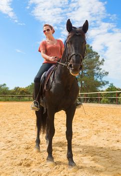 smiling riding girl and her black stallion in a training