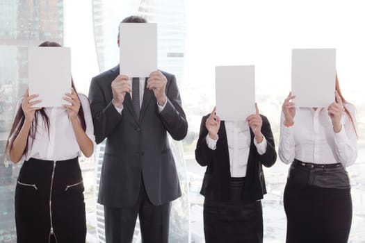 Portrait of business people group holding white papers and covering their faces