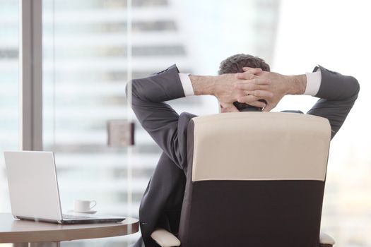 Businessman relaxes sitting in the office and looking in window