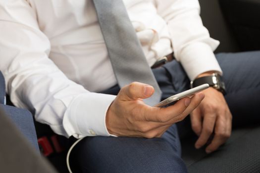 Close up of a businessman using smart phone while driving on the back seat of a car. Focus on mobile device.