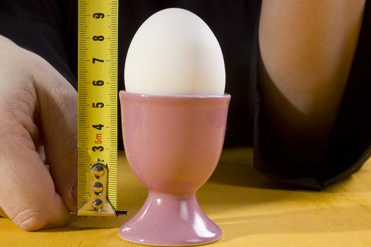 Egg in the holder and hands of the cook with a tape measure