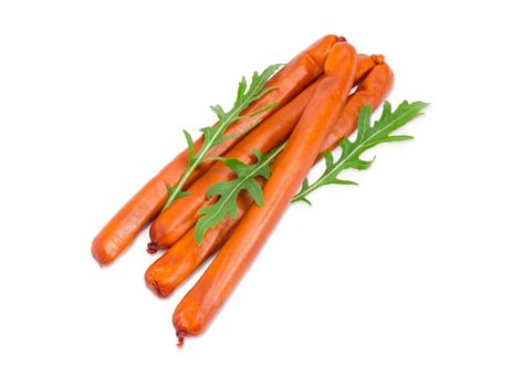 Several long thin smoked hunting frankfurters in the natural casing with several arugula leaves on a light background
