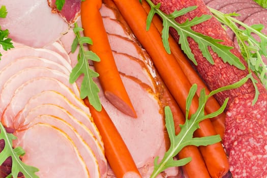 Background of the sliced boiled smoked pork loin and ham, partly sliced different salami, hunting sausages and other meat products with arugula and parsley 
