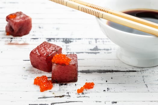 Tuna sashimi dipped in soy sauce with salmon roe on old white wooden board with chopsticks and bowl with soy. Raw fish in traditional Japanese style. Horizontal image.