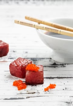 Tuna sashimi dipped in soy sauce with salmon roe on old white wooden board with chopsticks and bowl with soy. Raw fish in traditional Japanese style. Vertical image.