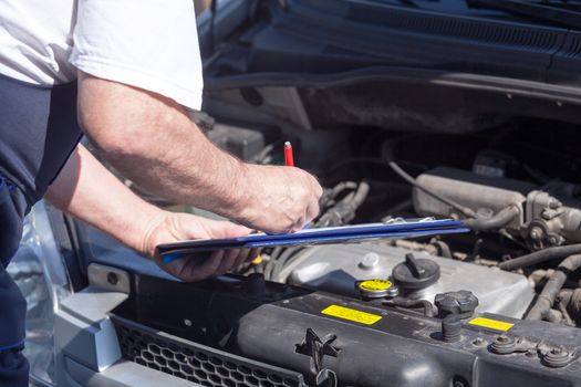 Auto mechanic checking car engine and writing on the clipboard