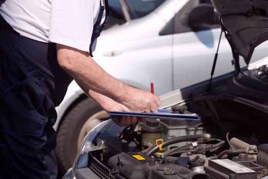 Auto mechanic checking car engine and writing on the clipboard