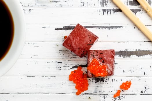 Tuna sashimi dipped in soy sauce with salmon roe on old white wooden board with chopsticks and bowl with soy viewed from above. Raw fish in traditional Japanese style. Horizontal image.