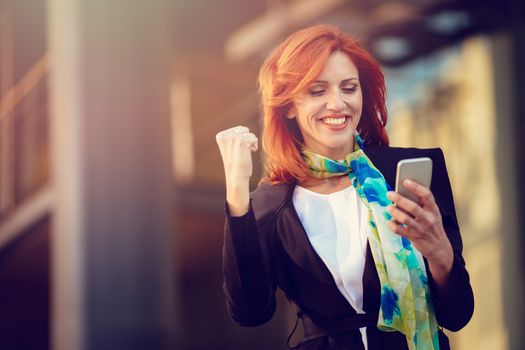 Smiling successful businesswoman using smartphone in office district.
