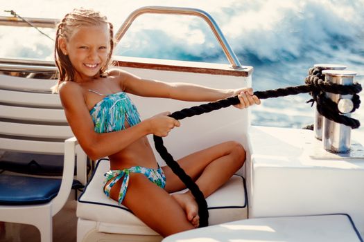 Cute smiling little girl enjoying on the deck. They are on cruise and sunbathing.