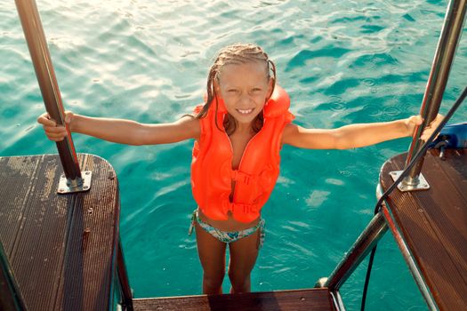 Cute smiling little girl with swim vest posing on sailing boat. 