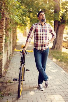 Casual businessman going to work by bicycle. He is walking next to bike and thinking.