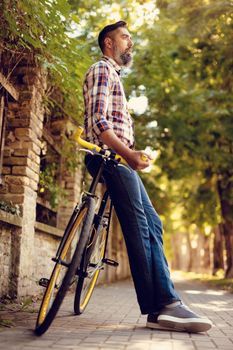 Casual businessman going to work by bicycle. He is standing next to bike and thinking.