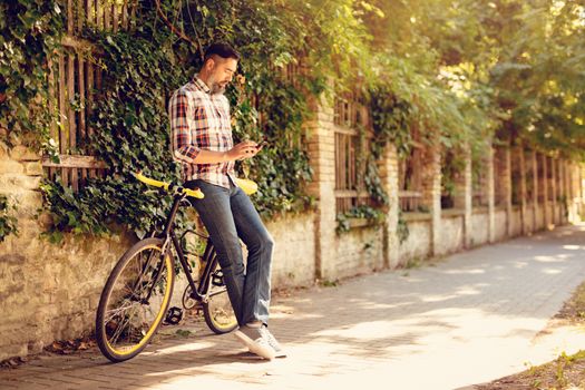 Casual businessman going to work by bicycle. He is standing next to bike and sending text message.